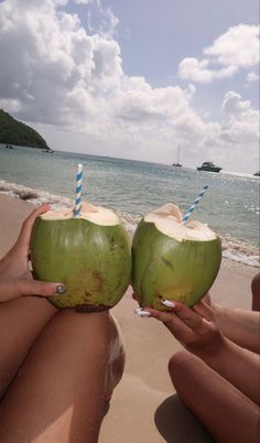 two people sitting on the beach holding up coconuts