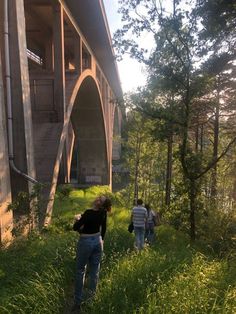 two people walking in the grass under a bridge