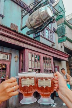 two people holding up beer glasses in front of a building