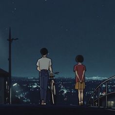 two people standing on top of a roof looking at the night sky with lights in the background