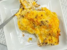 a white plate topped with a slice of cheese covered casserole next to a fork