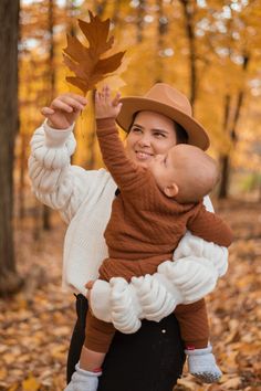 a woman holding a baby in her arms while wearing a brown hat and white sweater