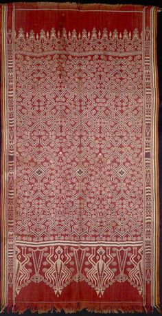 an old red and white cloth with intricate designs on the border, hanging from a black wall