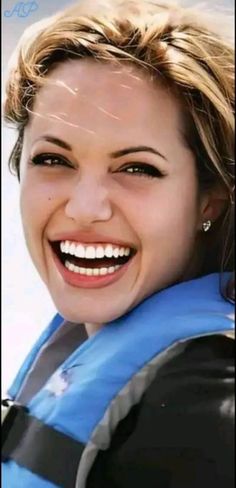 a close up of a person wearing a life jacket and smiling at the camera with an ocean in the background