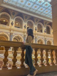 a woman standing on top of a balcony next to a stair case in a building