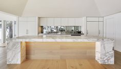 a kitchen with white cabinets and marble countertops in the middle of an open floor plan