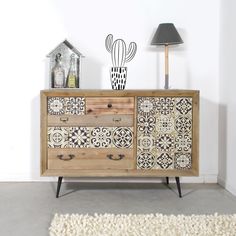 a wooden dresser with an artistic design on the front and side drawers, next to a lamp