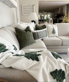 a living room filled with white couches covered in blankets and christmas tree throw pillows