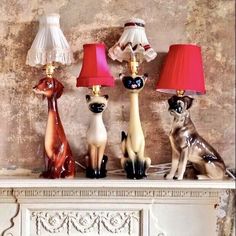 three ceramic cats sitting on top of a mantle next to two lamps and a lamp shade