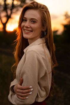 a woman with long red hair is smiling at the camera and has her hands on her hips