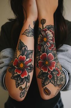 two women with tattoos on their arms holding hands up to their faces, both have flowers and leaves on them