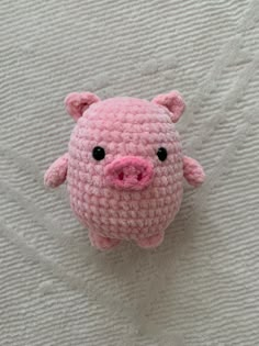 a small pink crocheted pig laying on top of a white bedding sheet