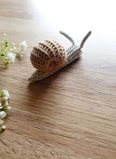 a crocheted snail sitting on top of a wooden table next to white flowers