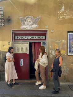 three women are standing in front of an old fashioned ticket machine, talking to each other