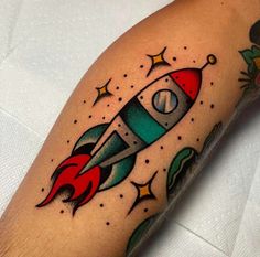 a tattoo on the arm of a man with a red and blue rocket ship in it