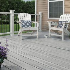 two white chairs sitting on top of a wooden deck next to a potted plant