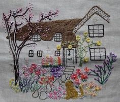 a house with flowers and a cat on the lawn in front of it is embroidered onto a piece of fabric