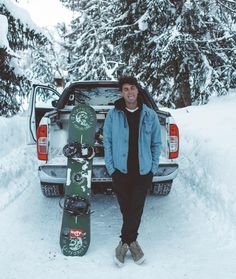 a man standing in the snow next to his truck with two snowboards on it