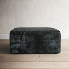 a black ottoman sitting on top of a hard wood floor next to a white wall