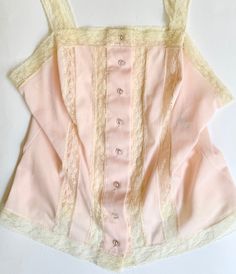 Adorable little vintage  50's/60's pale pink nylon button front camisole top with lace straps Made in USA 100% nylon Marked size 34 and photographed on a size 2/4 dress form. Please use measurements to ensure a proper fit. Pit-to-pit: 16" Top of shoulder-to-hem: 21-1/2" Good vintage condition A NOTE ABOUT MY CLOTHING LISTINGS: I'm very picky when it comes to cut and style so you can rest assured my vintage garments will be WEARABLE mixed in with your modern wardrobe.  I only source high-quality pieces in good to excellent condition and bring them to you at a REASONABLE price.  Unless otherwise noted, all garments are free of rips, tears, stains, missing buttons, etc. NOTE: Please bear that in mind that, when you purchase vintage, it might not be perfect, but it will be authentic.  No retur Fitted Pink Top With Delicate Lace, Fitted Pink Delicate Lace Top, Fitted Pink Camisole With Lace Top, Vintage Sleeveless Corset With Lace Trim, Pink Fitted Lace Top Camisole, Fitted Lace Top Pink Camisole, Vintage Sleeveless Lace Trim Corset, Vintage Lace Trim Sleeveless Corset, Fitted Vintage Camisole For Spring