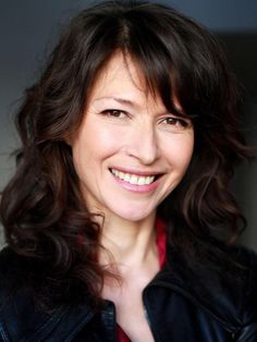 a smiling woman in a black leather jacket and red shirt is looking at the camera