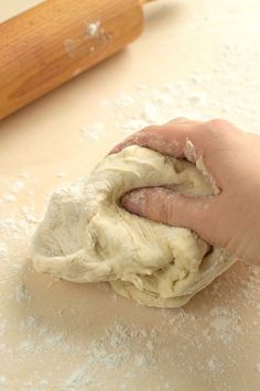 a person is kneading dough on a table with a rolling pin in the background