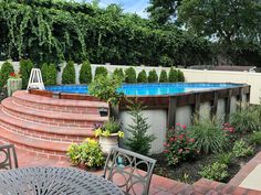 a backyard with a swimming pool surrounded by plants and flowers on the side walk way