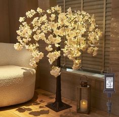 a lighted tree with white flowers in front of a window next to a candle holder