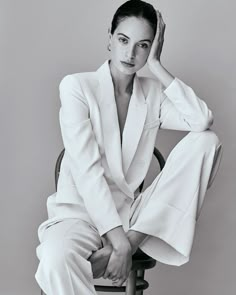 a black and white photo of a woman in a suit sitting on a chair with her hands behind her head