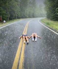 two people laying down on the side of a road in the middle of the woods