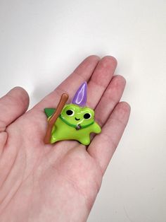 a hand holding a green toy with a purple hat