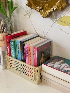 a stack of books sitting on top of a white counter next to a vase with flowers