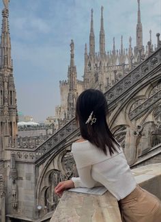 a woman sitting on top of a stone wall next to a building with spires