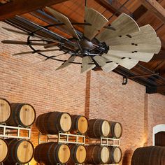 several wooden barrels are stacked up in a room with a fan hanging from the ceiling