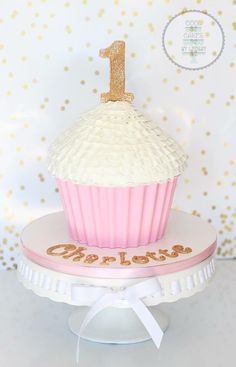 a pink and white cupcake with the number one on it is sitting on a cake stand