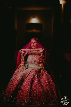 a woman in a red and gold wedding dress sitting on the floor with her veil draped over her head