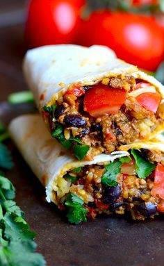 two burritos are stacked on top of each other with tomatoes in the background