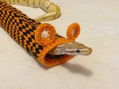 an orange and black knitted snake with its mouth open sitting on a white surface