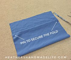 a pair of scissors laying on the ground next to a piece of blue cloth with pin to secure the fold