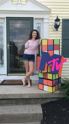 a woman standing next to a giant rubik cube on the front steps of a house