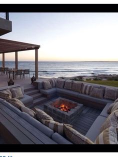 an outdoor fire pit with couches and pillows on the deck next to the ocean