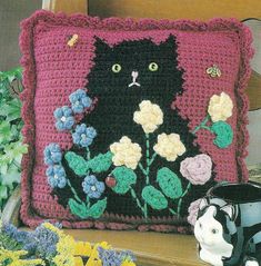 a crocheted pillow with a black cat on it and flowers in the background