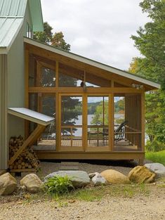 a small cabin with a porch and deck on the side of it, surrounded by rocks