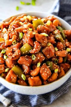 a white bowl filled with sesame seed chicken and green peppers on top of a blue towel