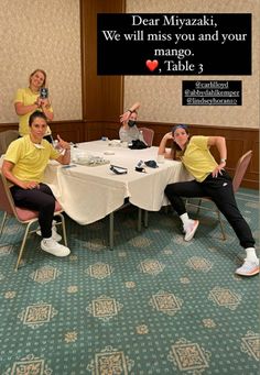 four people sitting at a table with drinks in front of them and one person holding up a cell phone