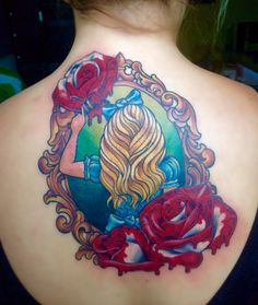 the back of a woman's shoulder with a tattoo on it, and roses around her neck