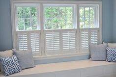 a window seat with pillows on it in front of a window that has white shutters