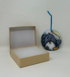 an ornament in a box with a bird on it and a blue ribbon