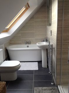 a white bath tub sitting next to a toilet in a bathroom under a slanted ceiling