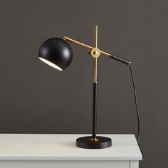 a black and gold desk lamp sitting on top of a white table next to a gray wall